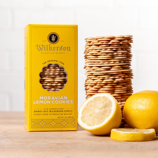 Yellow box of Wilkerson Moravian Lemon Cookies with cookies and lemons on a wooden surface.