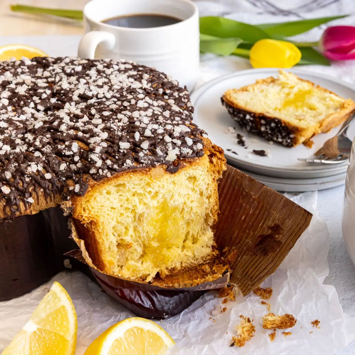 Baked goods with a slice cut, lemons, and a cup of coffee on a table.