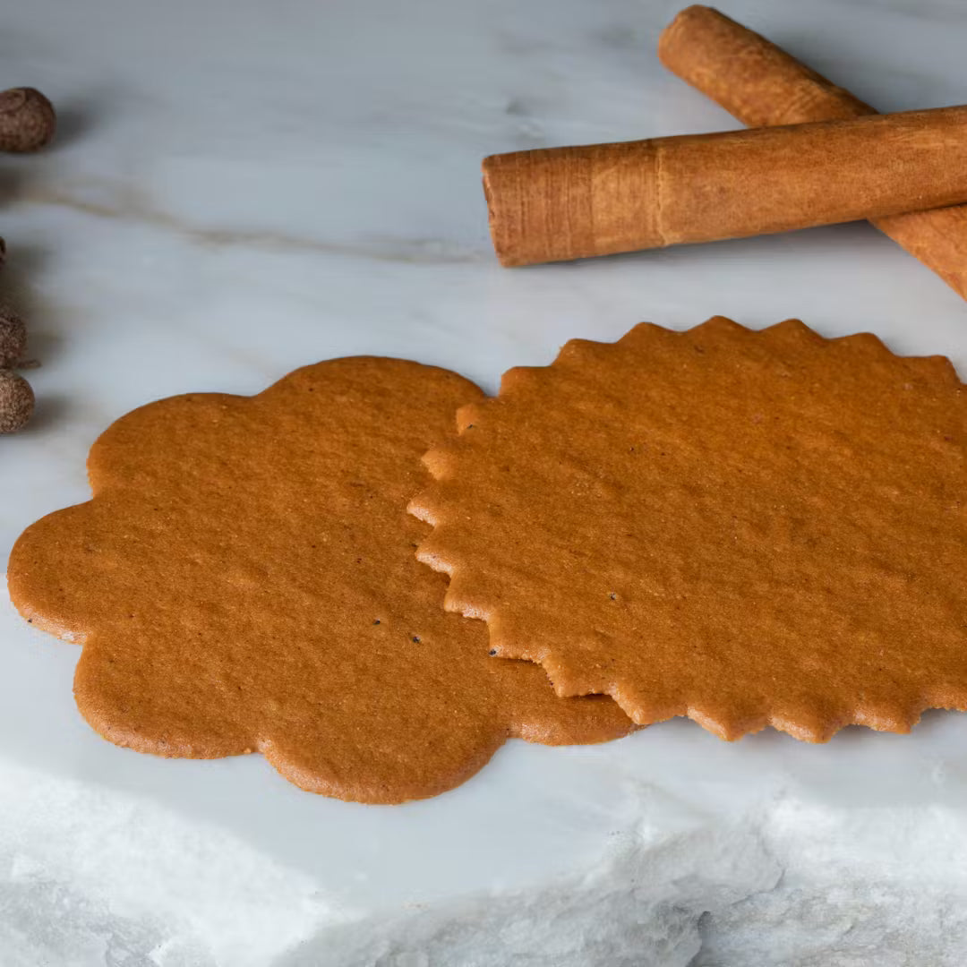 Two gingerbread cookies with a rolling pin and cinnamon sticks on a marble surface.