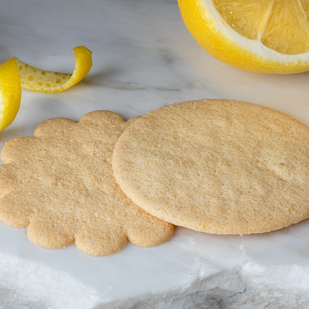 Two round cookies on a marble surface with lemon slices and peels.